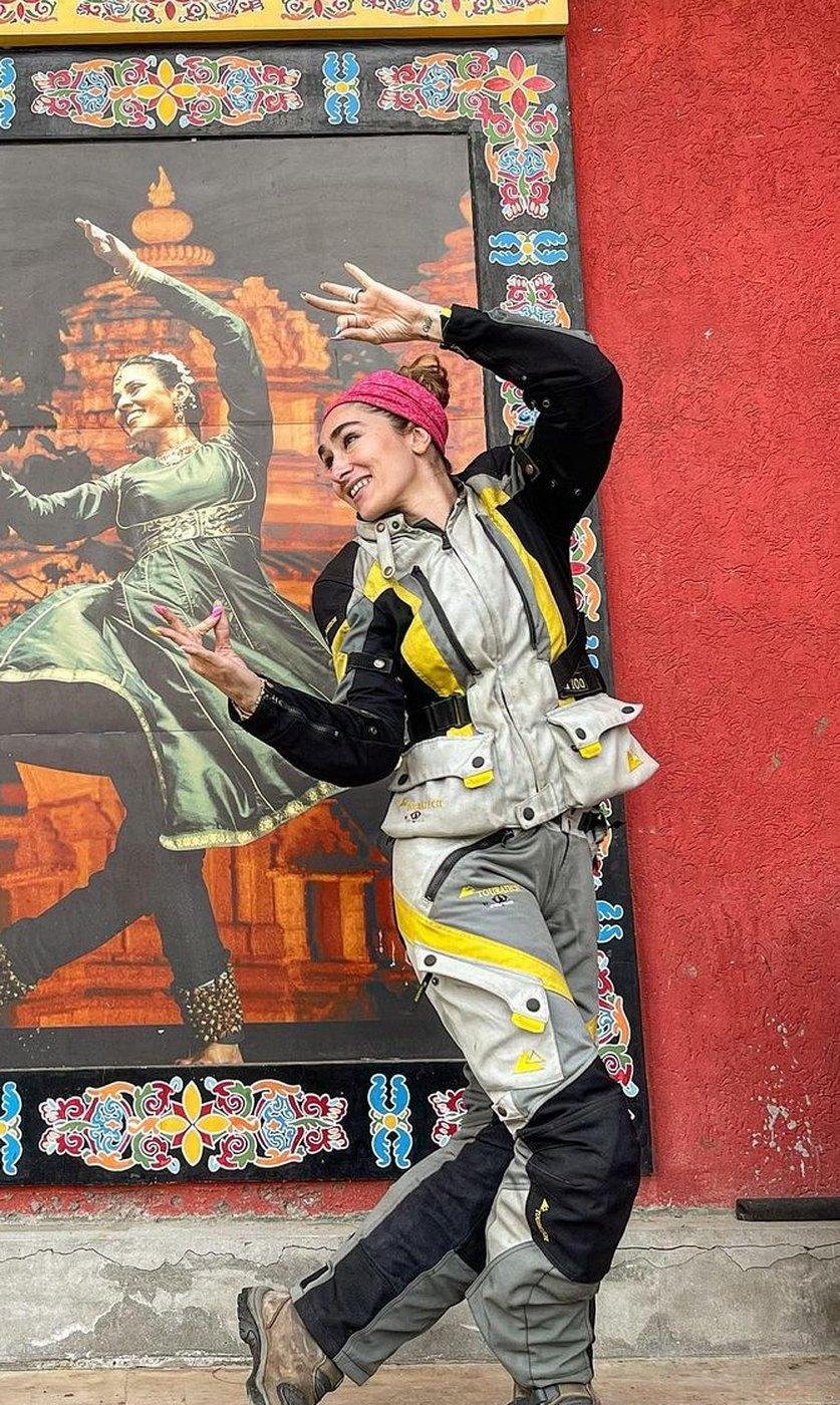 Maral Yazarloo in motorcycle touring gear, arms raised in front of a painted mural