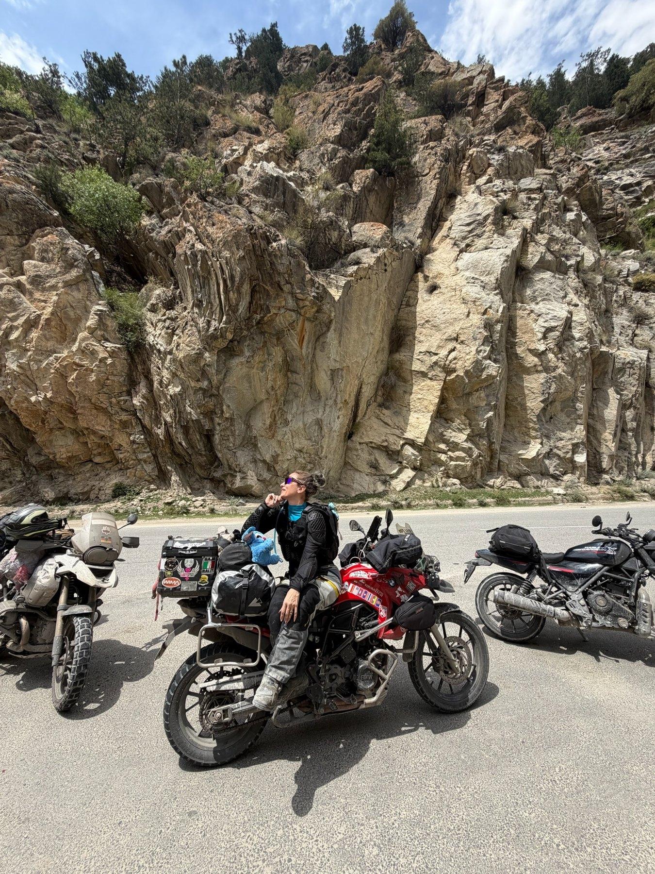 Maral Yazarloo resting on a loaded adventure motorcycle at a roadside rock face