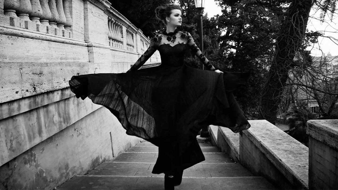 A black gown caught in motion on Roman steps